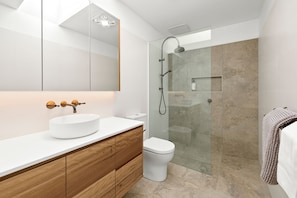 A modern bathroom with a white sink, wooden vanity, a glass shower enclosure, and a white toilet. - Bliss by the Beach (Aireys Inlet)