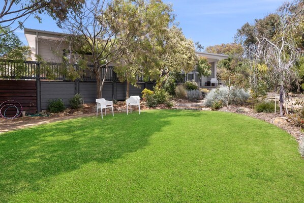 A well-maintained backyard with a lawn, a seating area with chairs, and a variety of plants and trees.