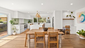 Een moderne keuken met witte kasten, een groot eiland en een eethoek met houten tafels en stoelen.