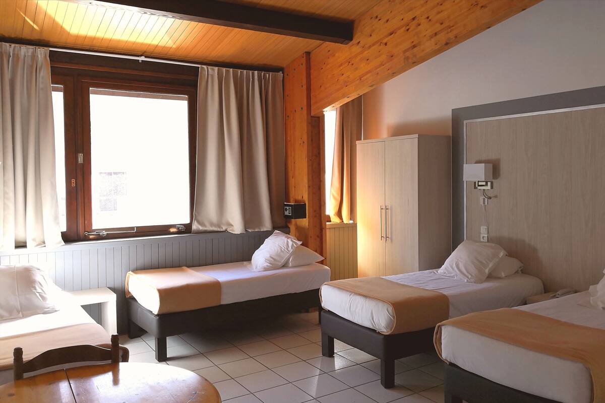 Een kamer met vier bedden, een houten plafond, een raam met gordijnen, een kledingkast en een nachtkastje.