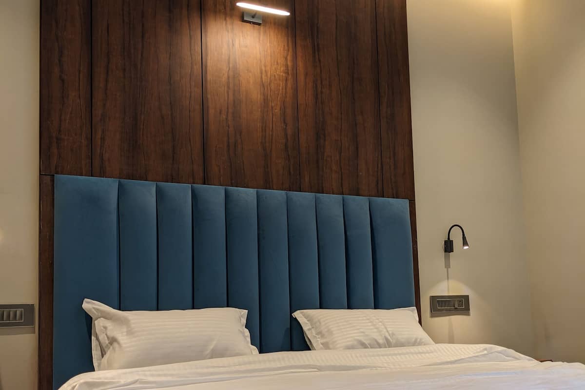 A neatly made bed with white linens and a blue upholstered headboard.