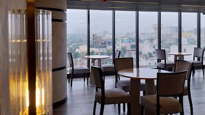 A modern dining area with round tables and chairs, large windows offering a city view, and a unique circular light fixture on the ceiling. - All Starr Sports (Jaipur)