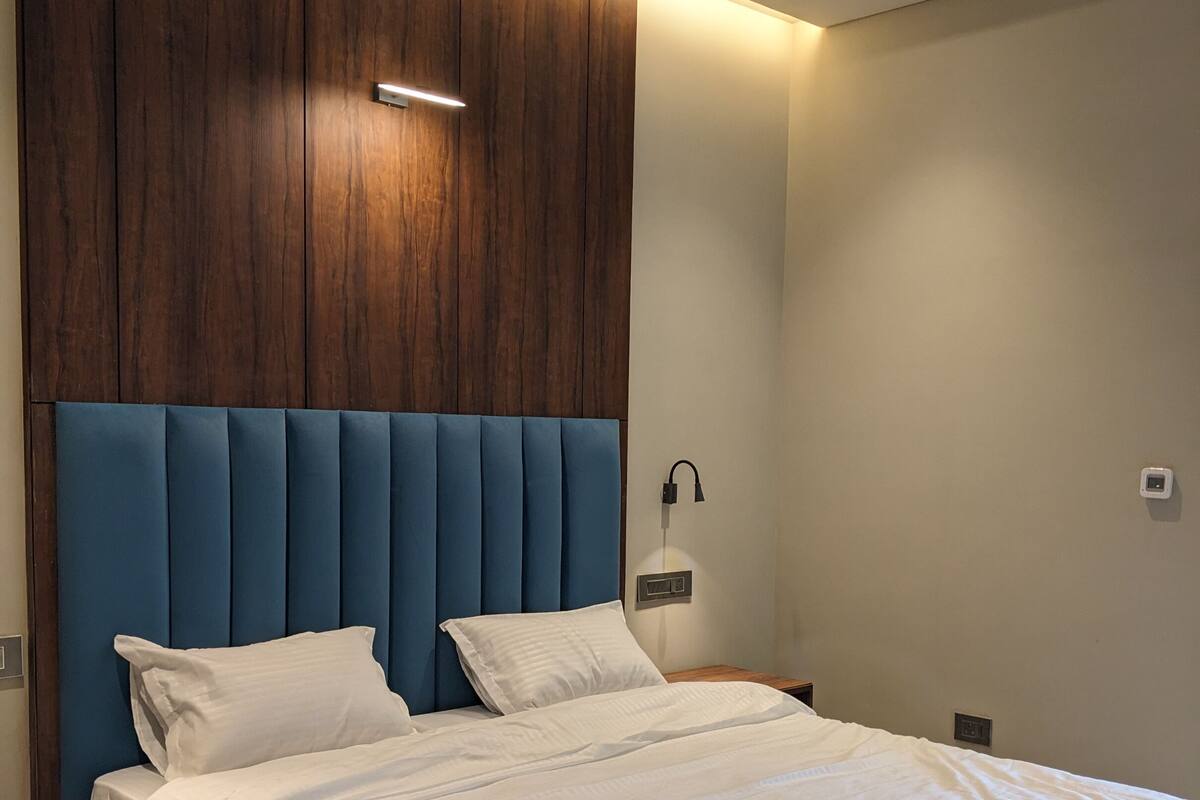 A modern bedroom with a large bed, wooden headboard, and a nightstand with a lamp.