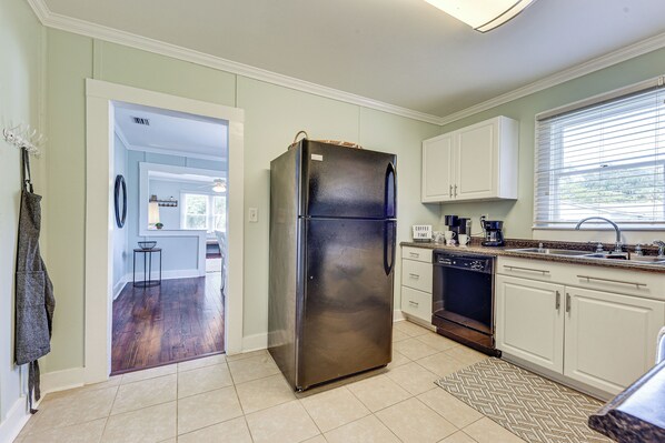 A kitchen with a stainless steel refrigerator, white cabinets, a dishwasher, and a window with blinds.