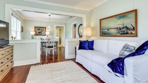 A living room with a white sofa, a blue throw blanket, and a painting of a coastal scene. - Dtwn St Marys Home Near Waterfront: Pets Welcome! (St. Marys)