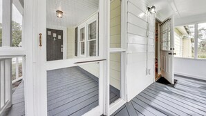 A covered porch with a wooden deck, white siding, and a door leading to a garage. - Dtwn St Marys Home Near Waterfront: Pets Welcome! (St. Marys)