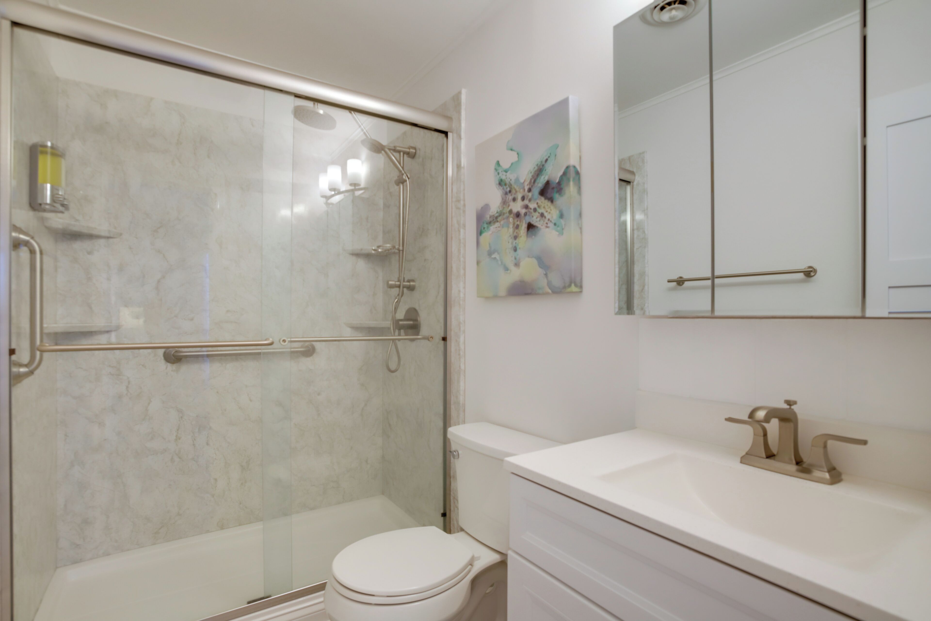 A modern bathroom with a glass-enclosed shower, a white toilet, and a sink with a gold faucet.