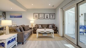 Un salon avec un canapé, une table basse et un tapis. Des tableaux encadrés ornent le mur et une lampe se trouve sur une table d’appoint.