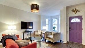 Ein Wohnzimmer mit Sofa, Sessel, Couchtisch, Fernseher und einer violetten Tür.