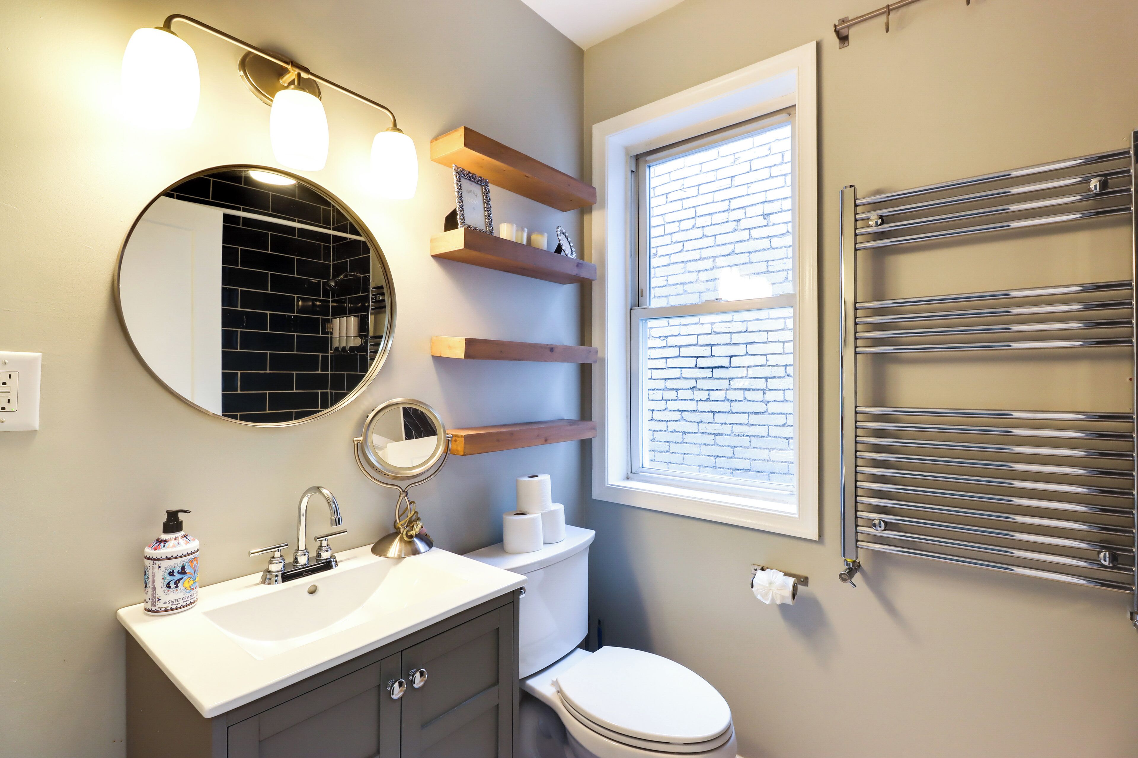 Une salle de bain avec un miroir rond, un lavabo, des toilettes et un porte-serviettes.