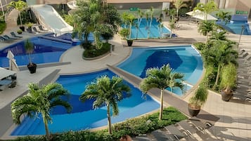 Un área de piscina con varias piscinas, palmeras y sillas de descanso.