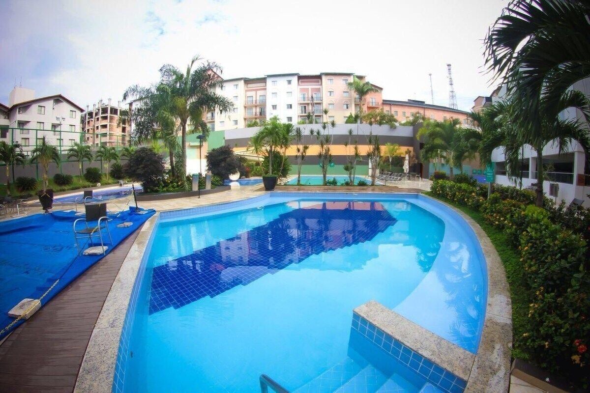 Piscina cercada por palmeiras e um edifício alto com varandas.