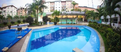 Piscina cercada por palmeiras e um edifício alto com varandas.