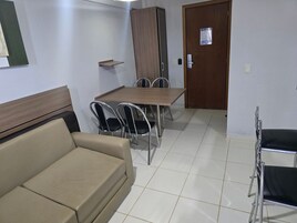 Una habitación pequeña y limpia con una mesa de madera, cuatro sillas, un sofá y un armario.