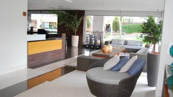 Een moderne hotel lobby met een receptiebalie, een zithoek met een bank en stoelen, en een groot raam met uitzicht op het omliggende landschap.