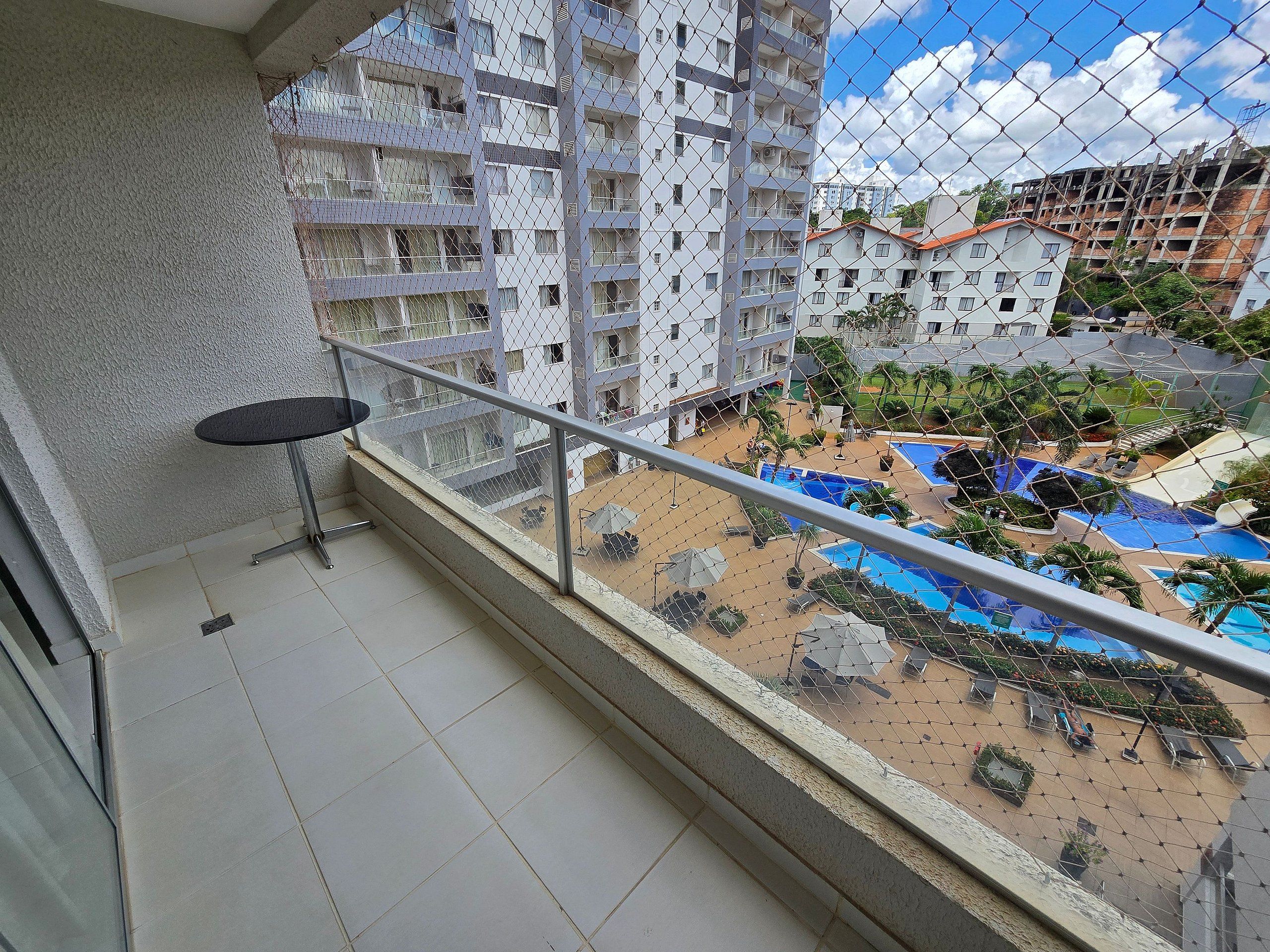 Un balcón con una mesa y vistas a una zona de piscina con palmeras.