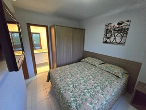 A bedroom with a bed, a wardrobe, and a bathroom visible through an open door. - Aptos Rio Quente - ótima área de lazer (Rio Quente)