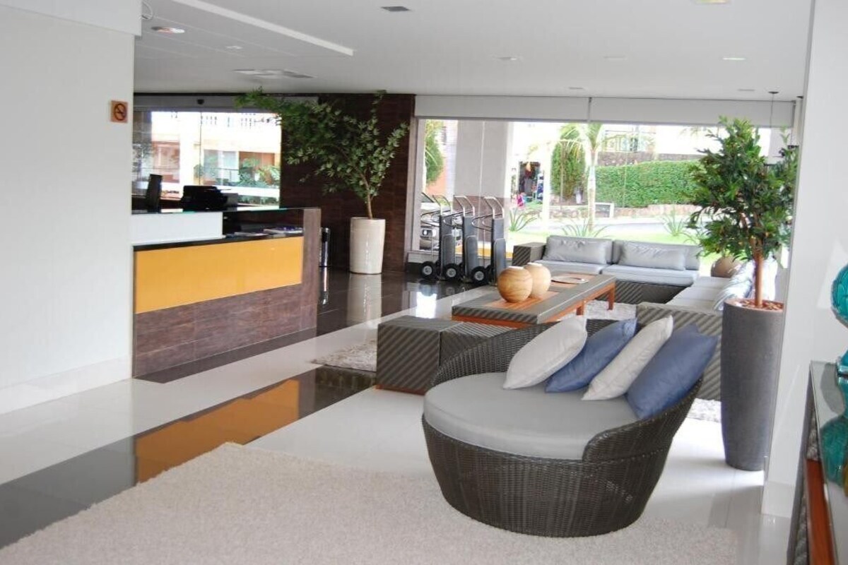 A modern hotel lobby with a reception desk, seating area, and large windows offering a view of the outdoors.