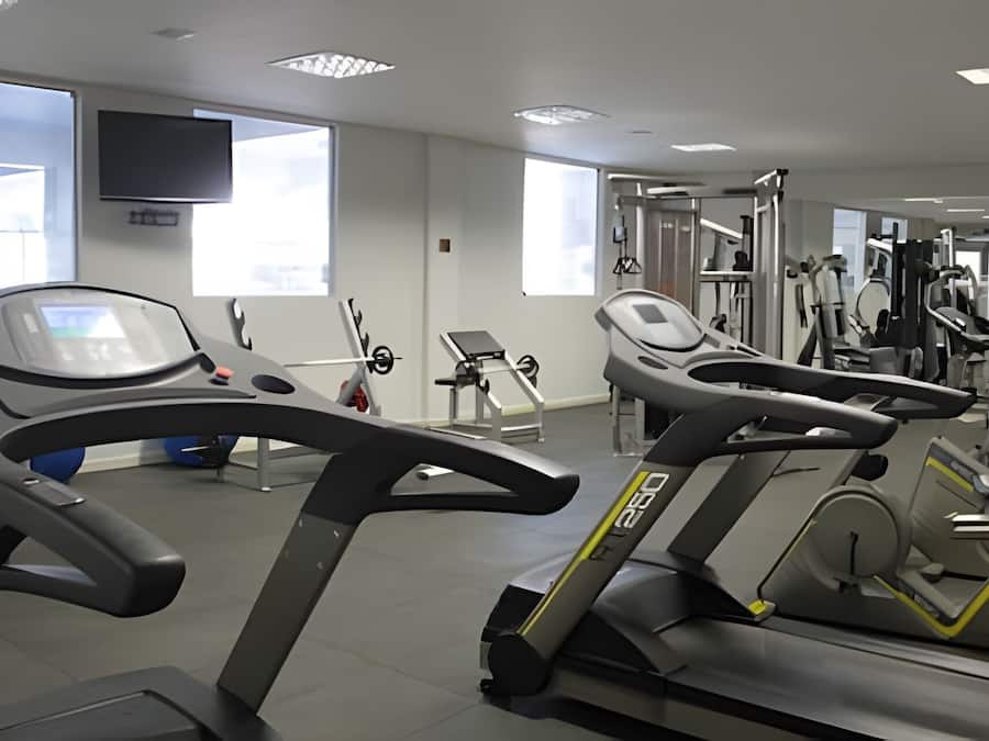 Un gimnasio con cintas de correr, máquinas de pesas y un televisor en la pared.