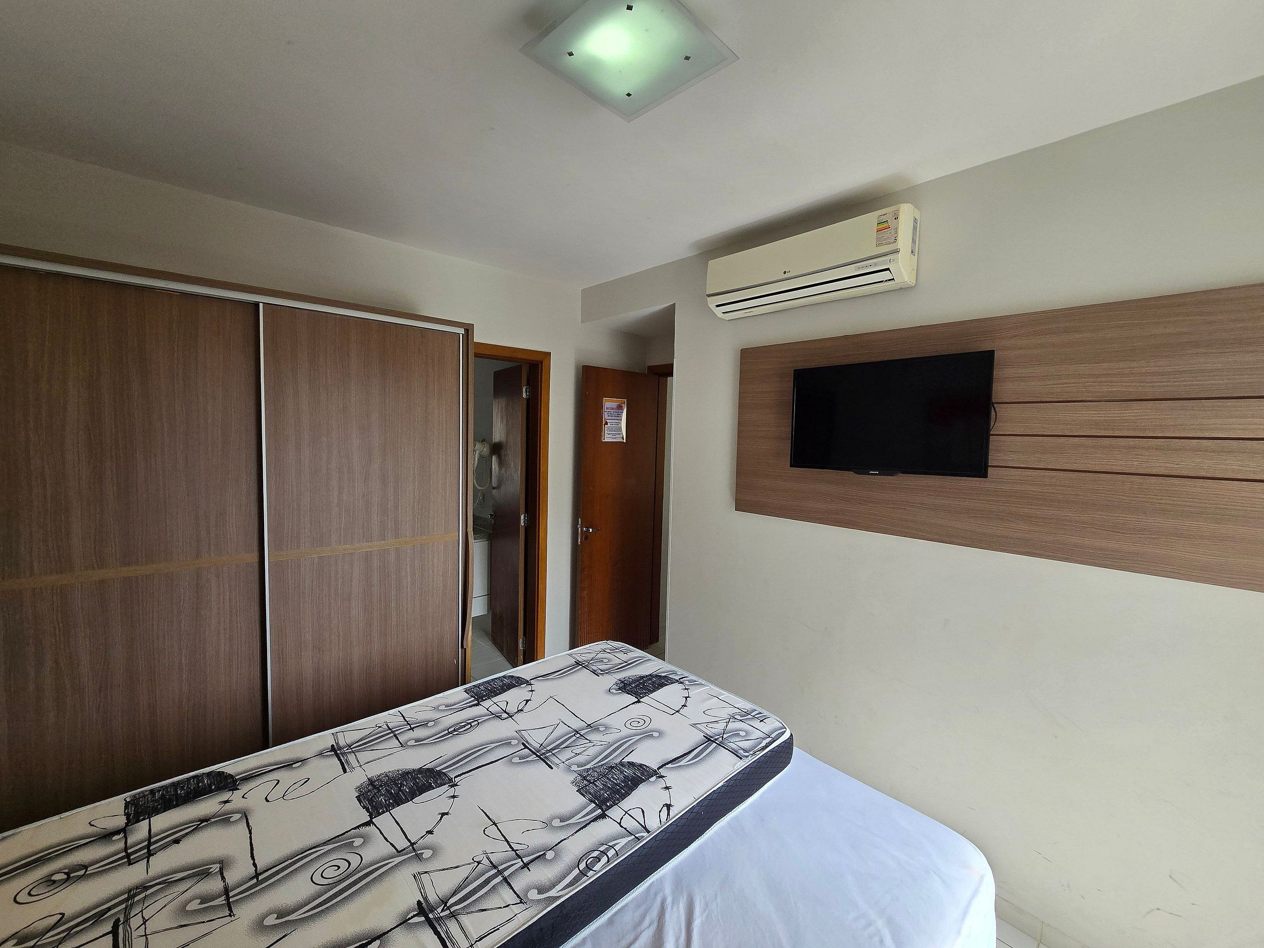 Un dormitorio con cama, armario, aire acondicionado y televisor de pantalla plana.