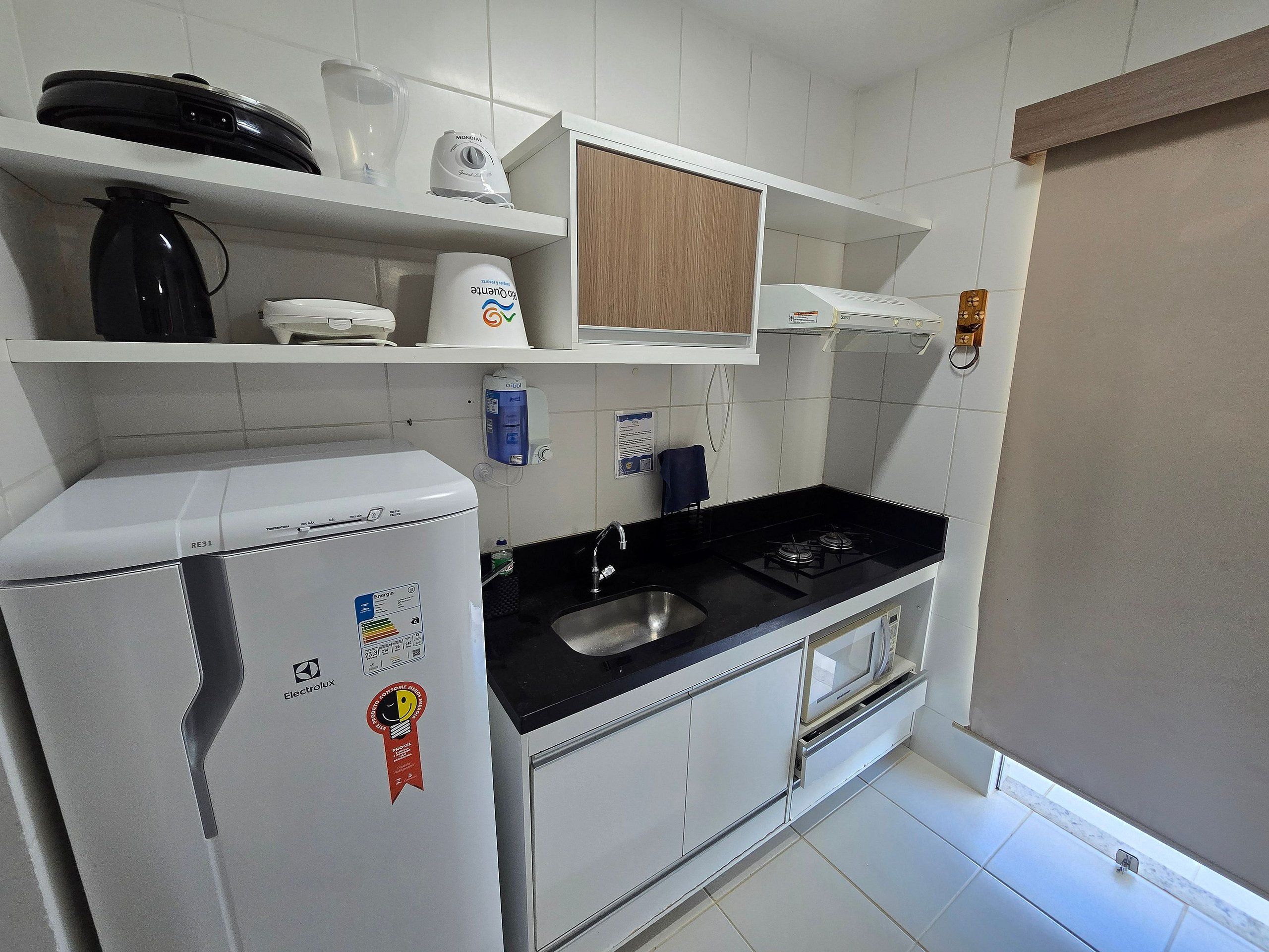 Een kleine keuken met witte kastjes, een zwart aanrecht, een ingebouwde magnetron en een klein spoelbakje.