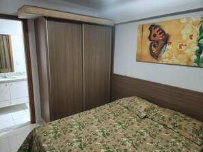 A bedroom with a bed, a wardrobe, a bathroom with a mirror, and a floral painting on the wall. - Aptos Rio Quente - ótima área de lazer (Rio Quente)