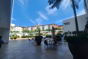 An outdoor patio area with tiled flooring, outdoor seating, and a view of multi-story buildings in the background. - Aptos Rio Quente - ótima área de lazer (Rio Quente)
