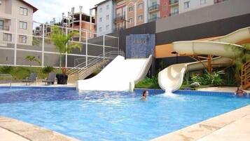Una piscina con tobogán de agua, rodeada por un edificio con balcones y un cielo despejado.