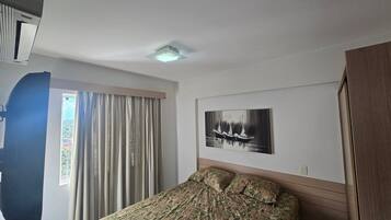 Un dormitorio con cama, ventana con cortinas, luz de techo y una obra de arte colgada en la pared.