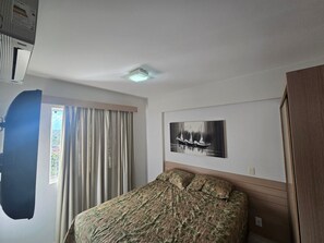 Un dormitorio con cama, ventana con cortinas, luz de techo y una obra de arte colgada en la pared.