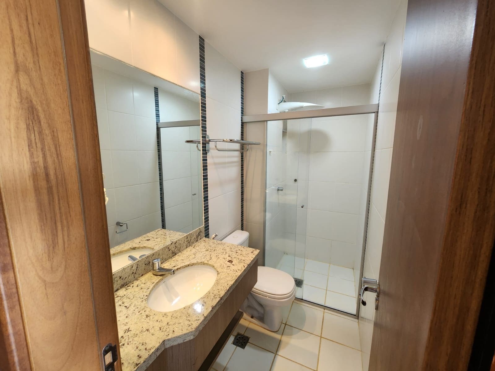 A bathroom with a granite countertop sink, a mirror, a toilet, and a glass shower enclosure.