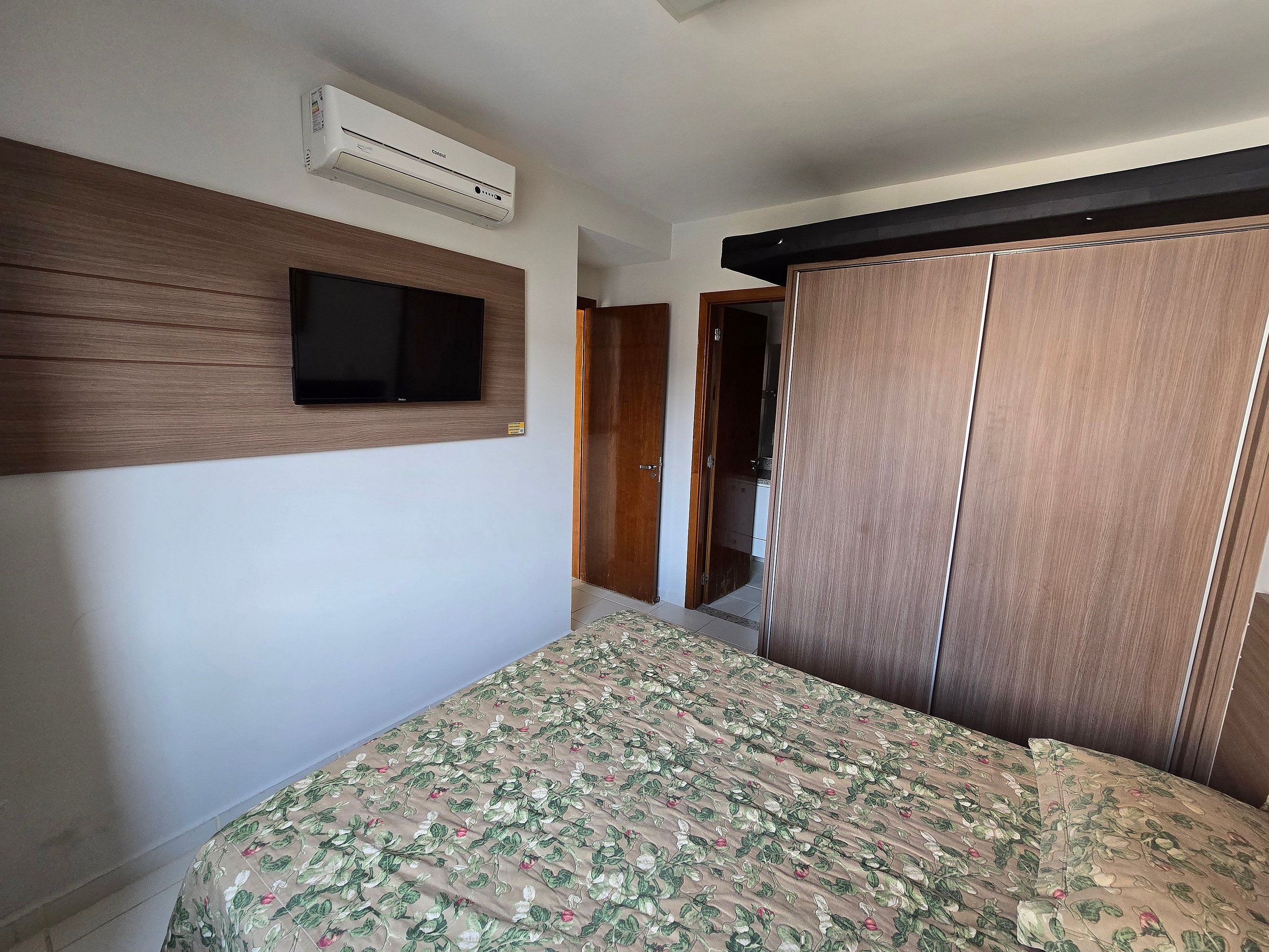Un dormitorio con cama, televisor montado, aire acondicionado y armario.