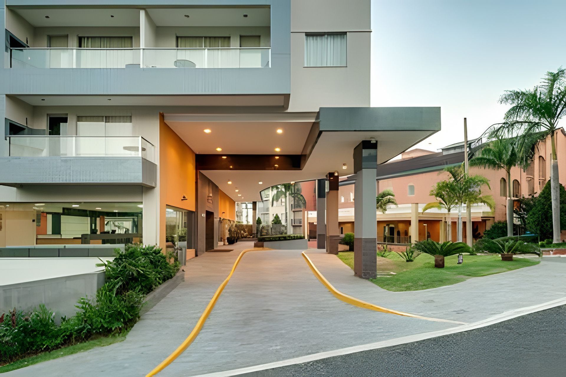 Uma entrada de hotel moderna, com galeria coberta, área de estar externa e um jardim bem cuidado.
