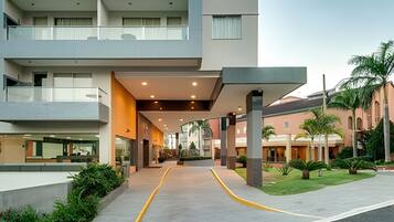 Uma entrada de hotel moderna, com galeria coberta, área de estar externa e um jardim bem cuidado.