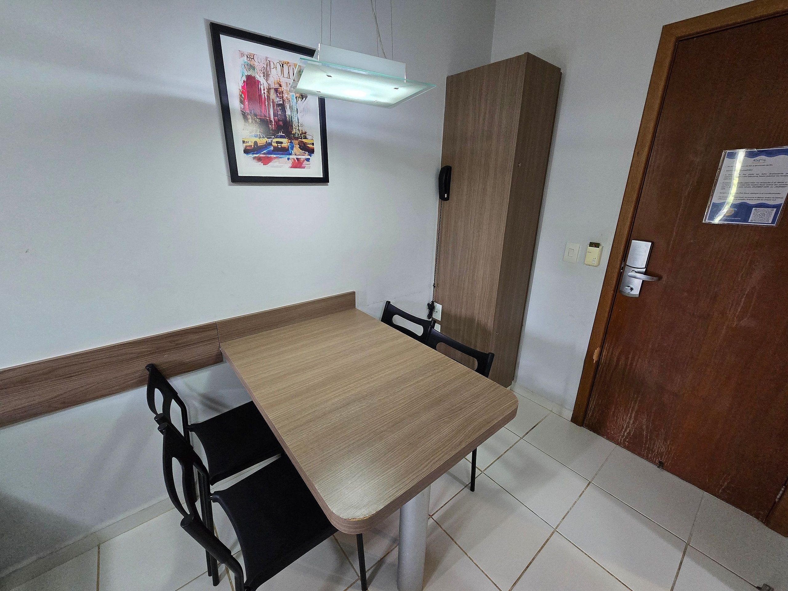 Une pièce avec une table et des chaises en bois, un tableau encadré au mur, un meuble et une porte avec une pancarte.