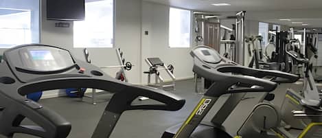 A gym with treadmills, weight machines, and a TV on the wall.