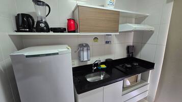 Una cocina compacta equipada con refrigerador, cafetera, hervidor y microondas.