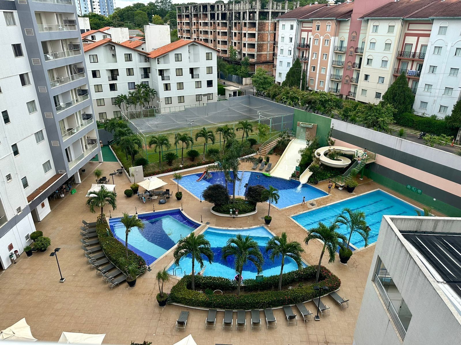 Un área de piscina en la azotea con múltiples piscinas, palmeras y sillones de descanso.