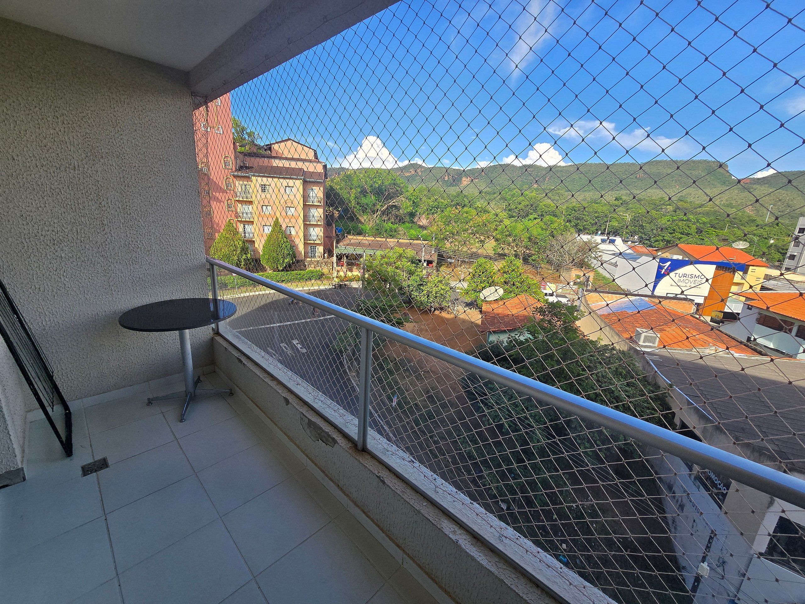 Un balcon donnant sur un paysage montagneux, une petite table et une clôture en treillis métallique.