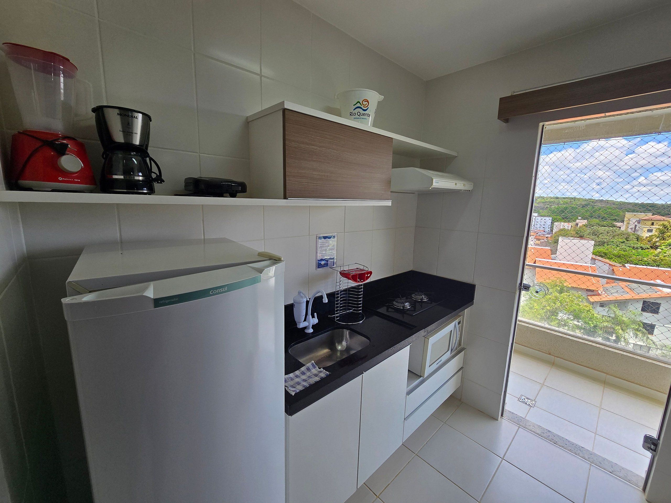 Cocina con refrigerador, estufa y cafetera. Se ve una ventana con vistas a edificios y árboles.