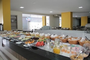 Un bufé con diversos alimentos y bebidas, dispuestos en una mesa larga con cestas y fuentes.