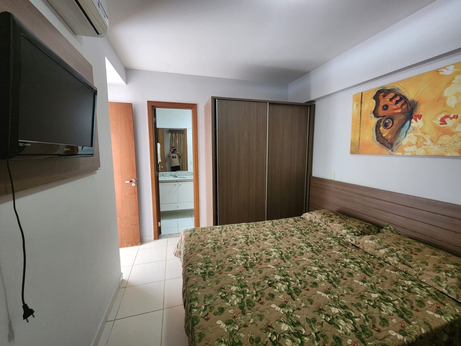 Un dormitorio con cama, televisión, armario y un cuadro en la pared.