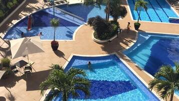 A rooftop swimming pool area with multiple pools, lounge chairs, and palm trees.