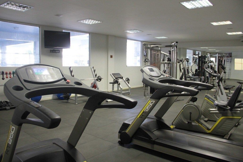 Un gimnasio con cintas de correr, máquinas de pesas y un televisor en la pared.