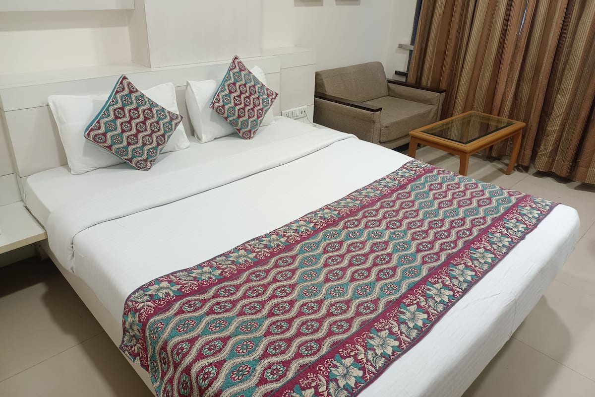 A neatly made bed with patterned pillows, a small side table, and a chair in a modern room with a white color scheme.
