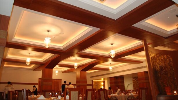 Un espace repas agrémenté de poutres en bois au plafond et d’un éclairage encastré. Les tables sont dressées avec des nappes et des bougies.