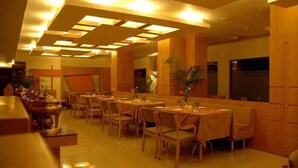 Un restaurant avec plusieurs tables et chaises, un plafond doté d’un éclairage encastré et une cuisine située au fond de la salle.