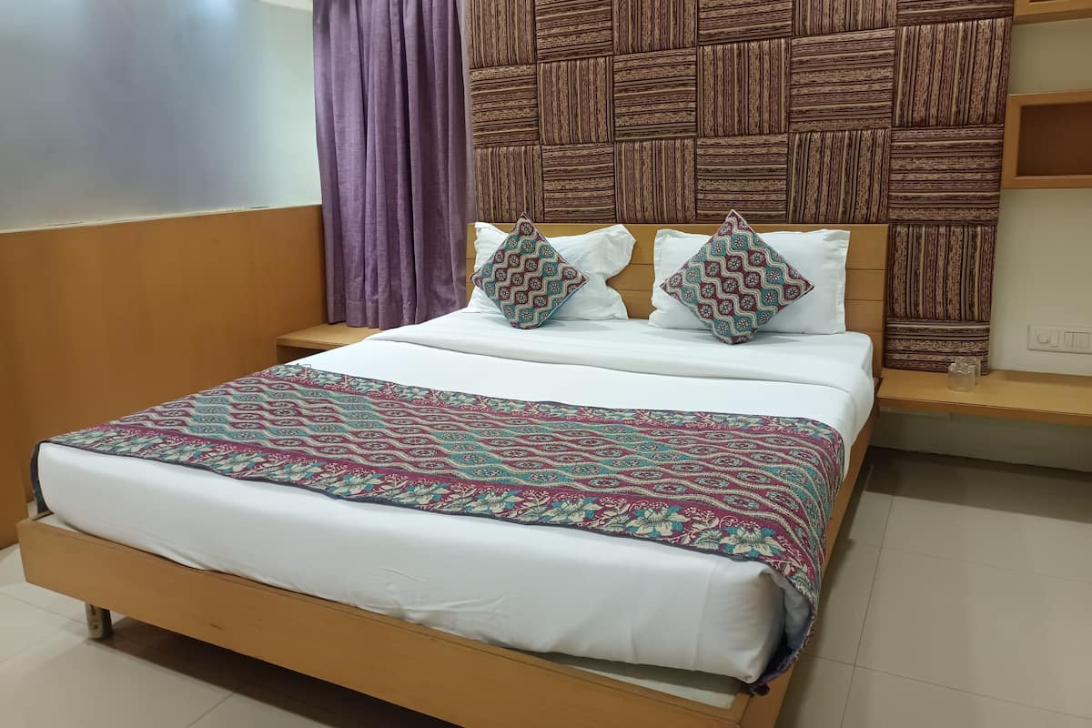 A bed with a patterned bedspread, two decorative pillows, a wooden headboard, and a nightstand with a glass container.