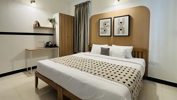 Habitació d'hotel moderna amb llit, taula de nit, armari i dues làmpades fixades a la paret.