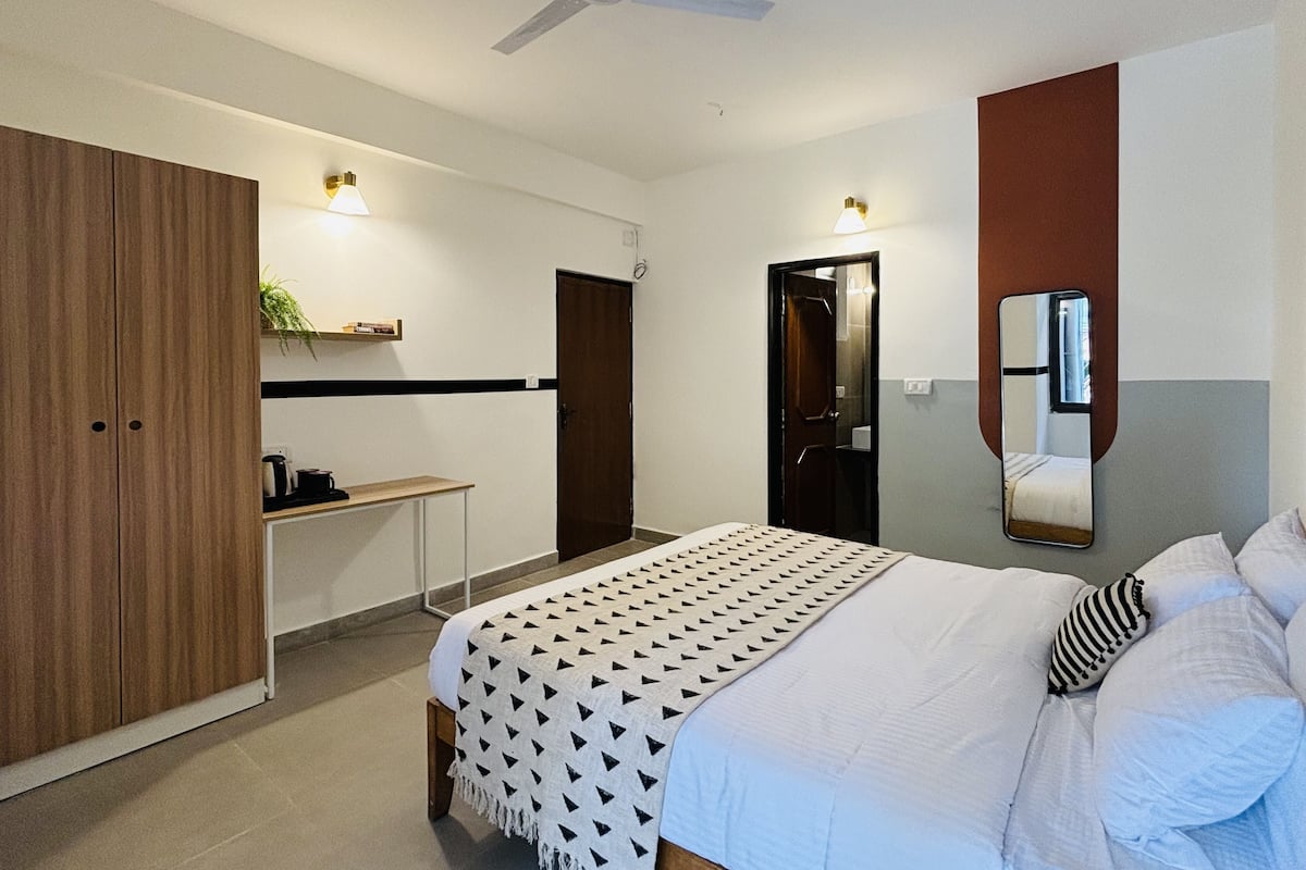 A bedroom with a bed, bedside table, wardrobe, ceiling fan, and a mirror.
